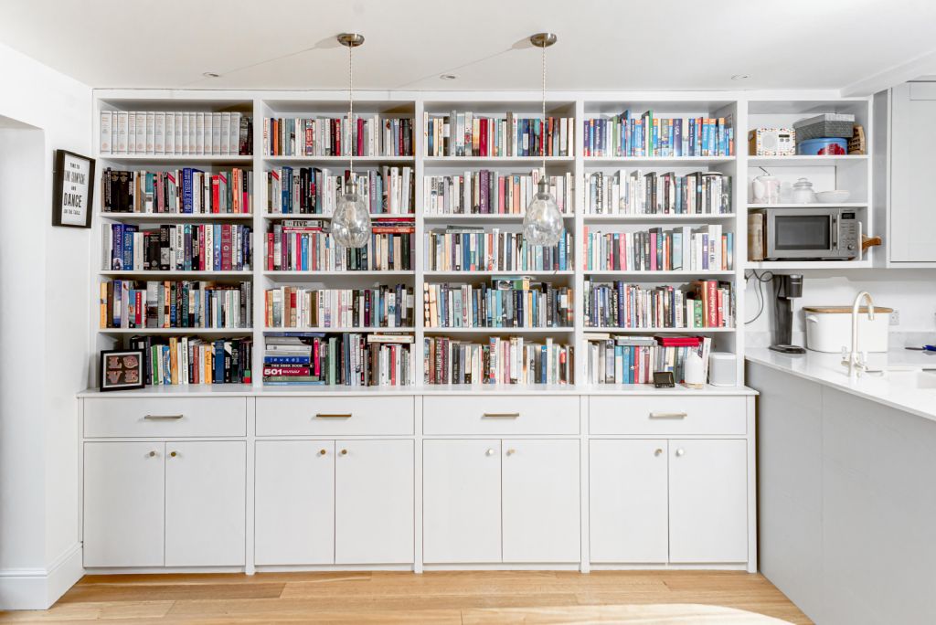 Large wall to wall built-in bookshelf with cupboards at the bottom next to kitchen.