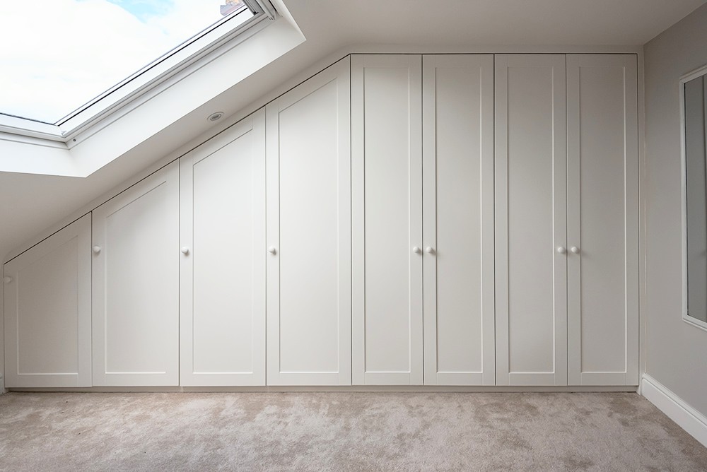 Large wall to wall built-in wardrobe on slanted wall with 8 doors in loft bedroom