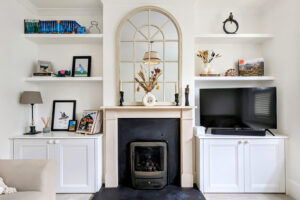 Two built-in alcove cupboards next to fireplace in Victorian house with floating shelves on either side of alcove units