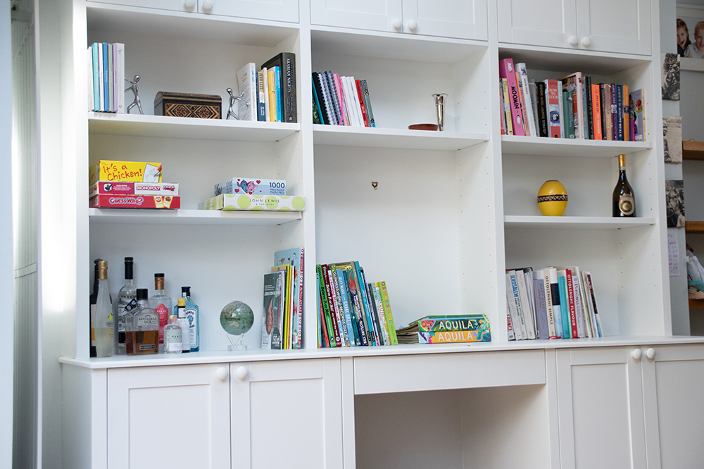 White cupboard with built-in shelving to store large books and ornaments.