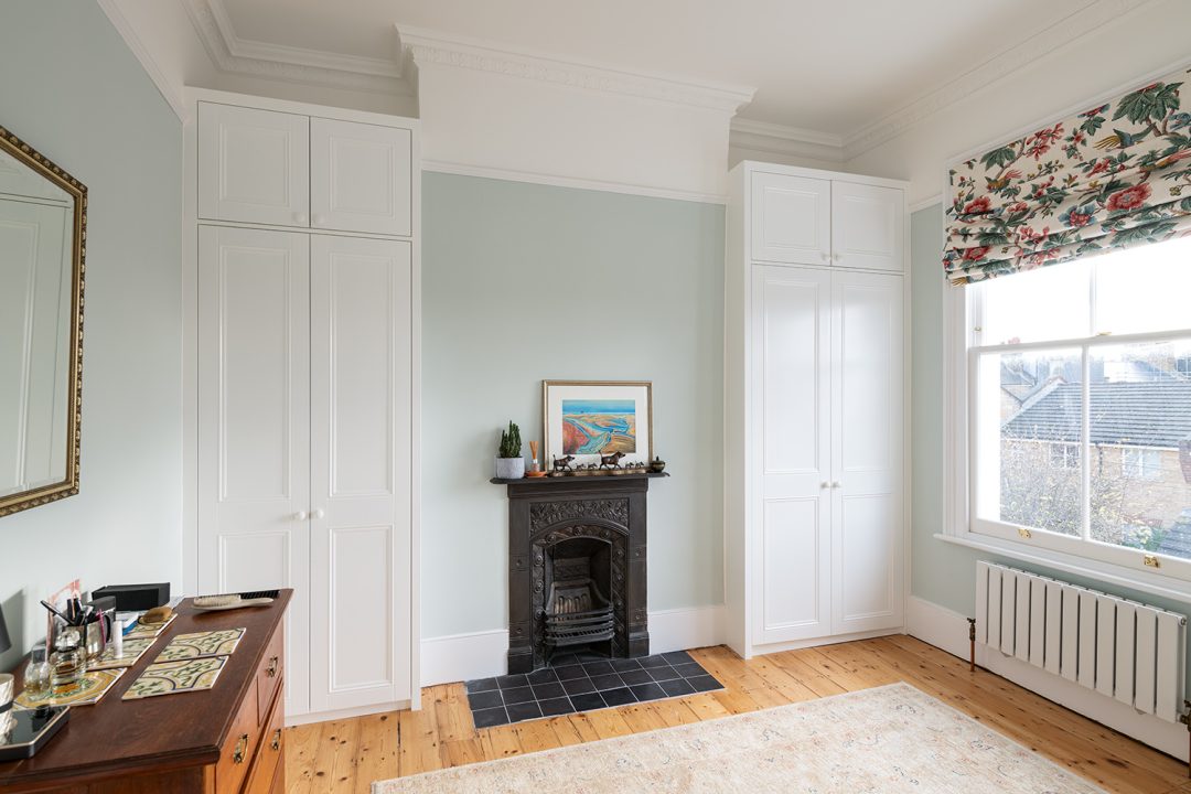 2 white alcove wardrobes in bedroom next to fireplace.