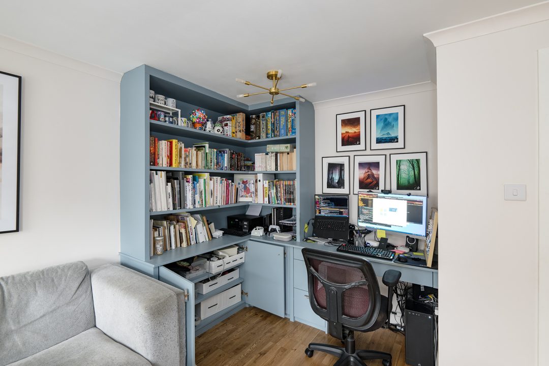 Blue built in home office with desk, cupboards and shelving unit.