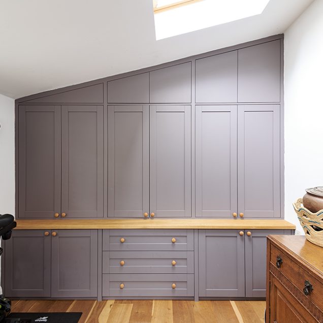 Large grey wall to wall built-in loft wardrobe with 6 doors and cupboards at the bottom. Designed and installed by Bespoke Carpentry London